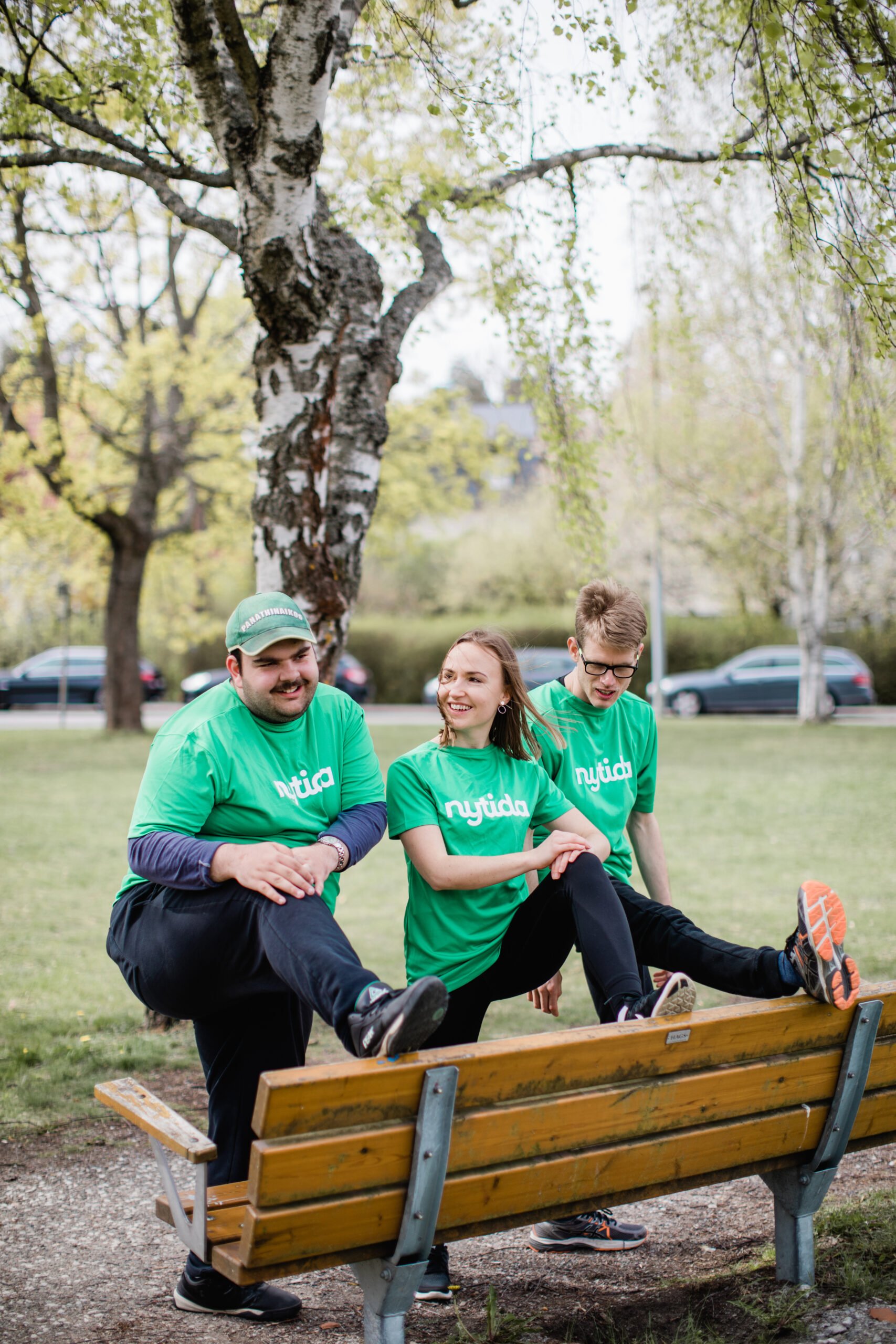 tre personer med gröna tröjor med text Nytida stretchar mot parkbänk