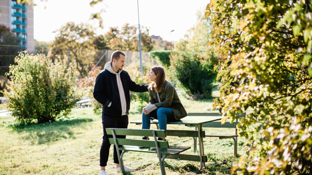 Man stöttar kvinna som sitter ihopkrupen på en parkbänk