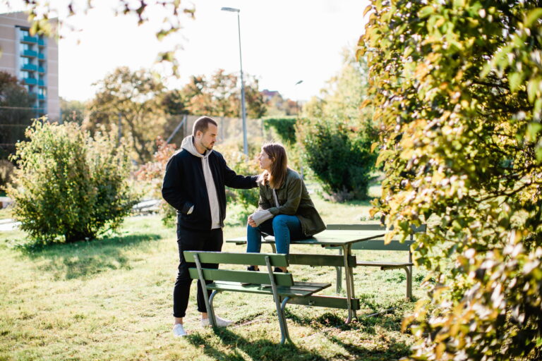 Man stöttar kvinna som sitter ihopkrupen på en parkbänk